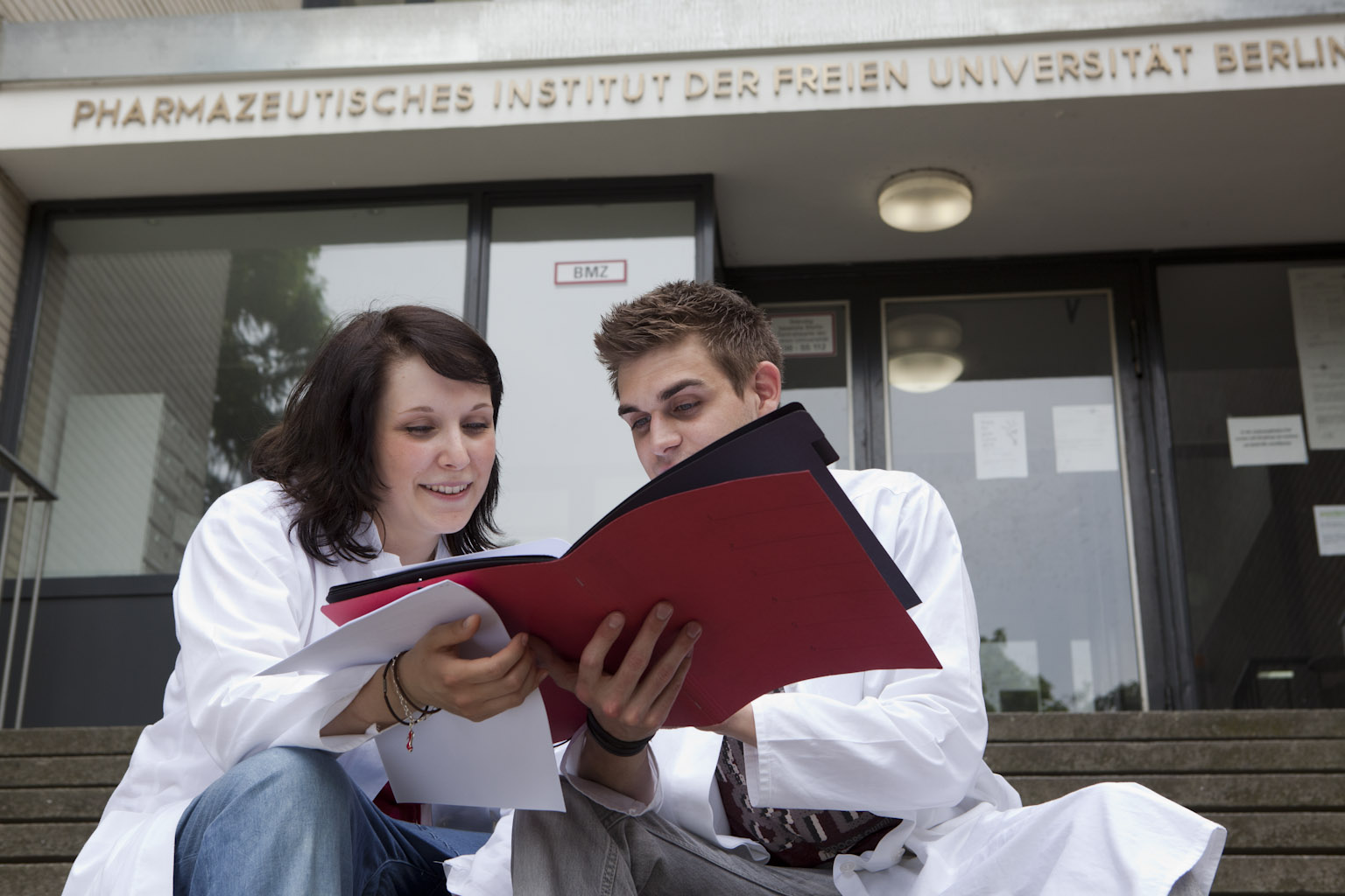 Pharmaziestudierende sitzen in Unterlagen lesend vor der Uni Berlin