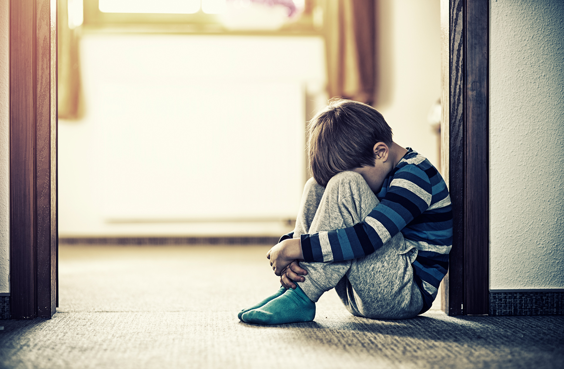 Ein trauriges Kind sitzt im Türrahmen mit Kopf zwischen den Beinen