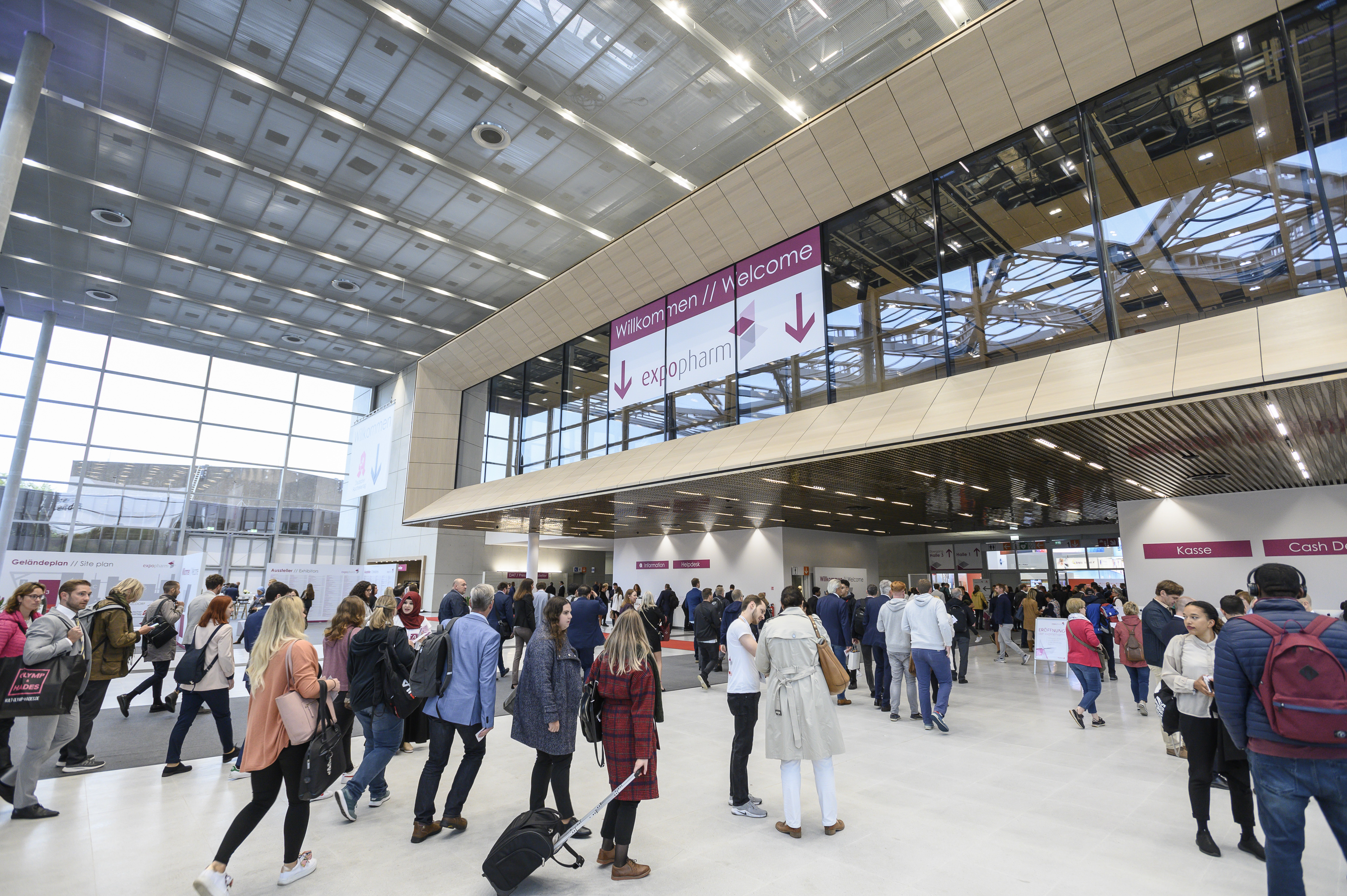 Auf dem Bild sieht man den Eingangsbereich der Messe Düsseldorf. Dort findet die expopharm 2023 statt. Im Eingangsbereich sind sehr viele Menschen, die zur expopharm gehen.