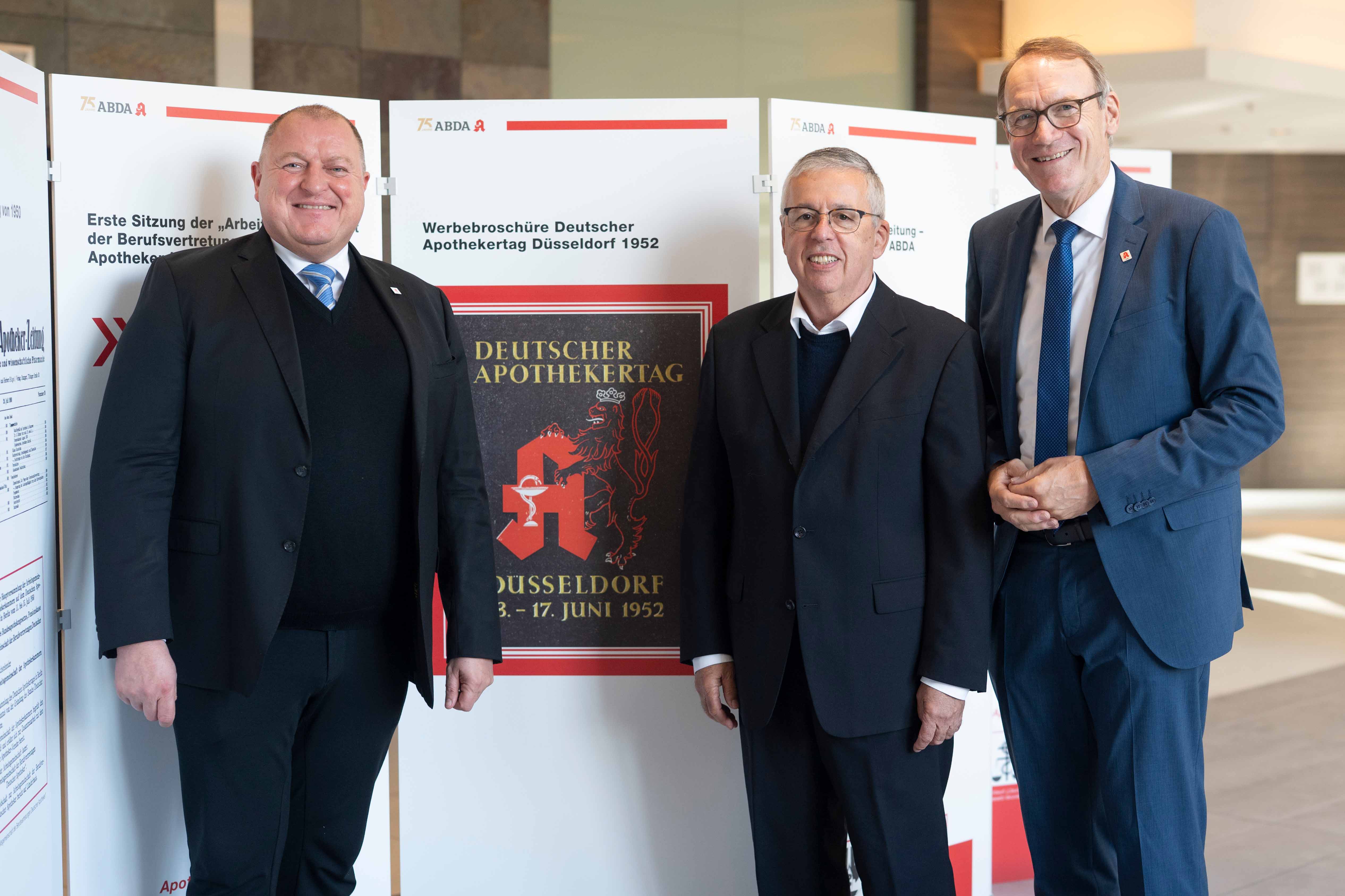 Dr. Armin Hoffmann, Dr. Holger Goetzendorff und Thomas Preis stehen vor den Ausstellungstafeln. Zu sehen ist die Werbebroschüre Deutscher Apothekertag Düsseldorf 1952.