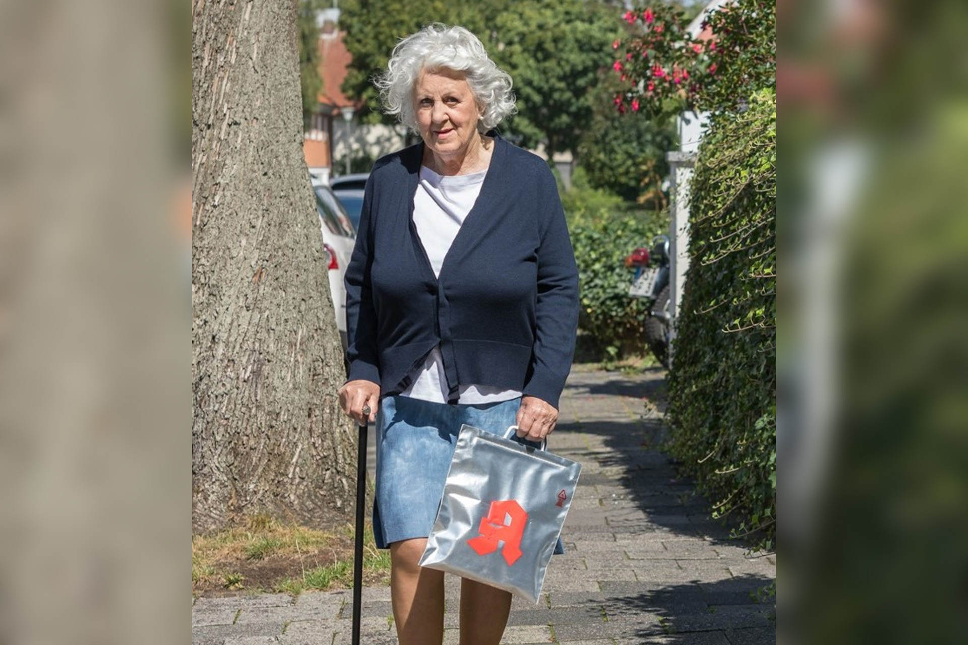 Eine ältere Frau auf einem Gehweg mit Apotheken-Einkaufstüte, die vor Hitze schützt