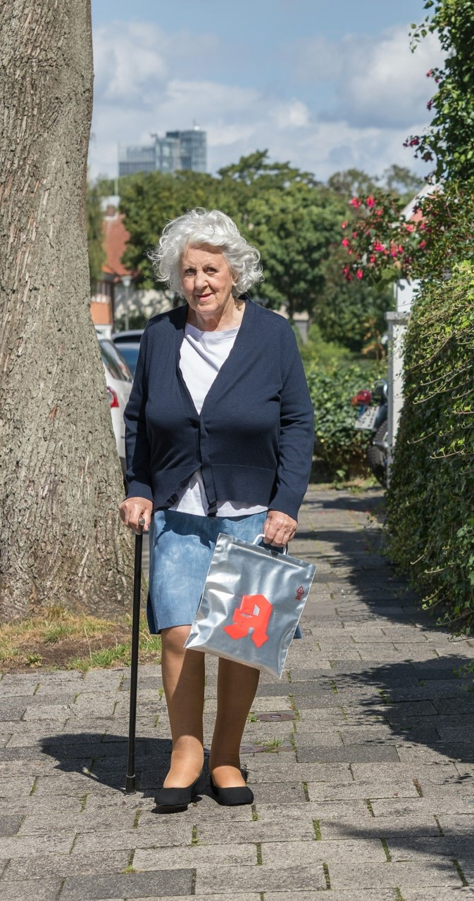 Eine ältere Frau auf einem Gehweg mit Apotheken-Einkaufstüte, die vor Hitze schützt