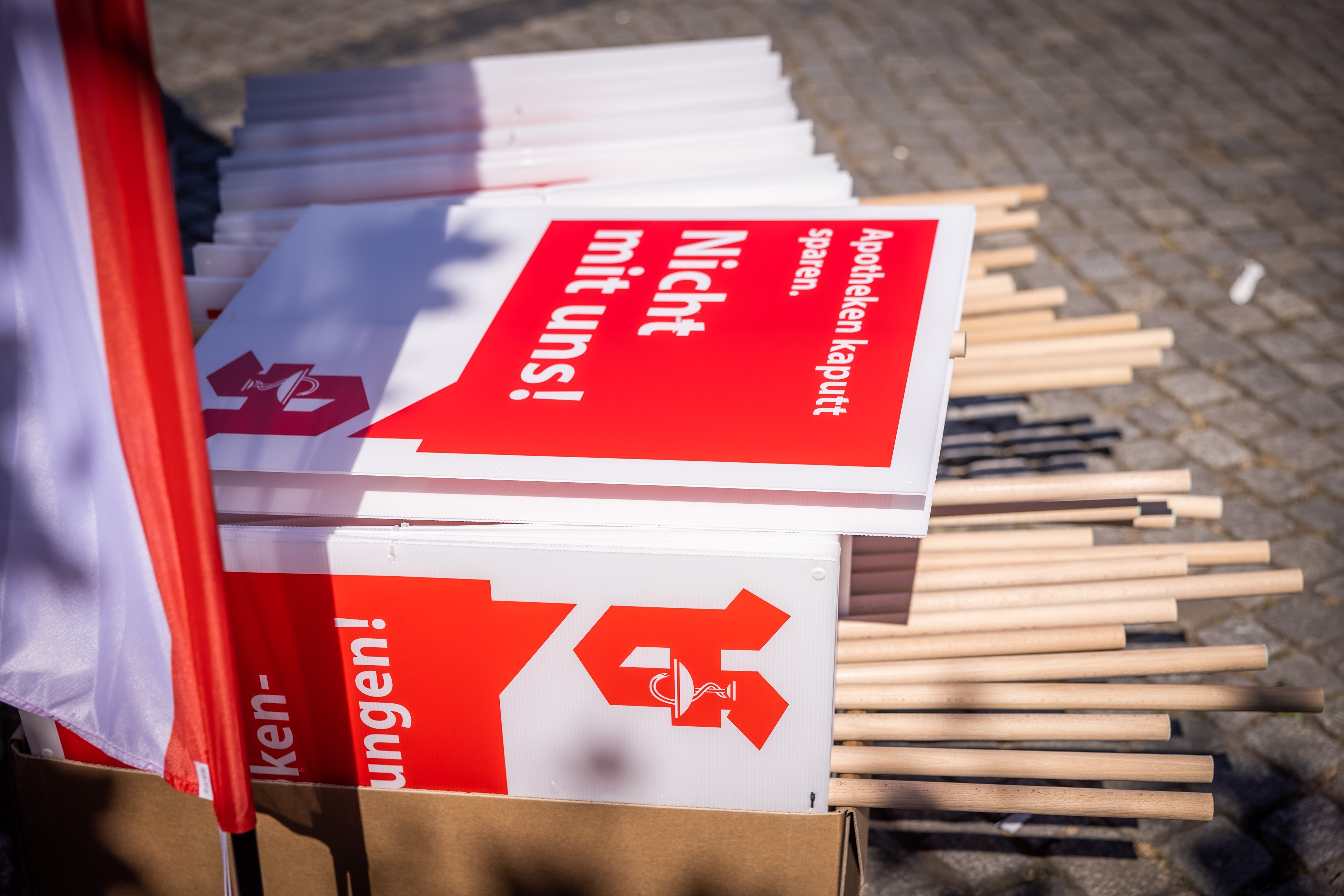 Unzählige Protest-Schilder liegen auf einem Stapel bereit für die Demonstration. Auf den Schildern steht geschrieben: "Apotheken kaputt sparen. Nicht mit uns!" Darunter befindet sich das Apotheken A.