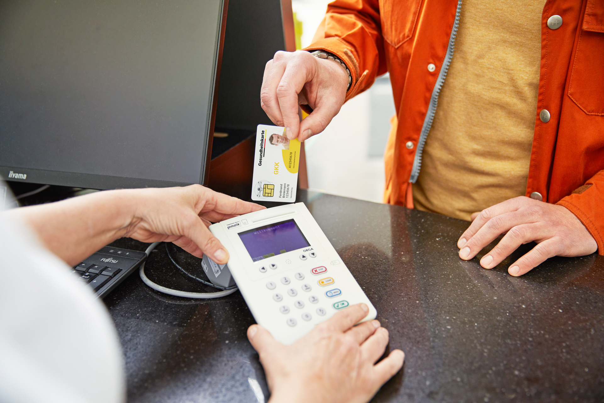 Ein Patient steckt in der Apotheke seine EGK in ein Terminal der Apothekerin