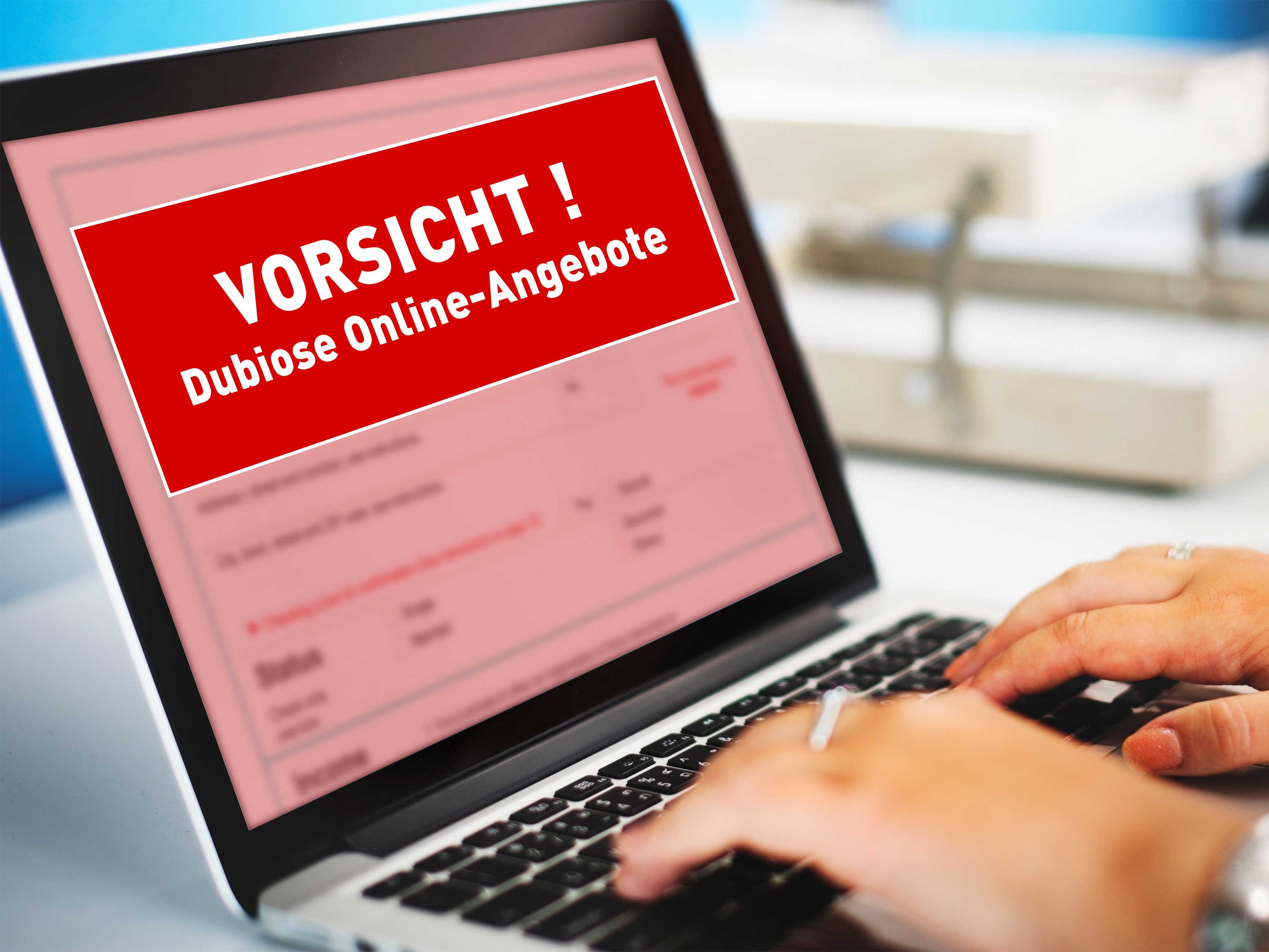 Person tippt auf einem Laptop. Auf dem Bildschirm ist eine Internetseite unscharf dargestellt und mit einem roten Warnhinweis überlagert. Der gut sichtbare Text lautet: „VORSICHT! Dubiose Online-Angebote“. Das Bild symbolisiert die Warnung vor unseriösen oder betrügerischen Angeboten im Internet.